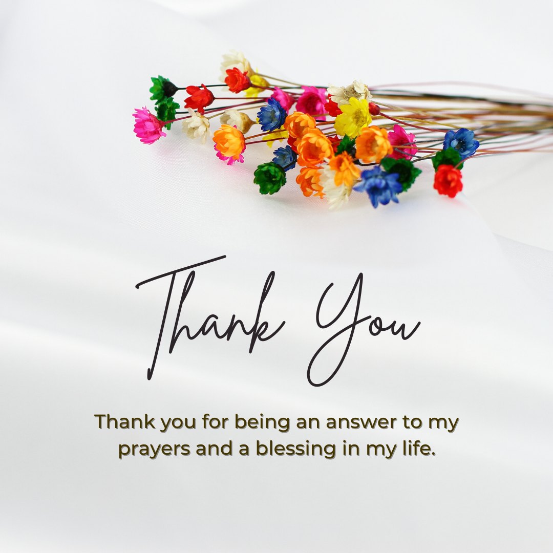 Simple yet elegant thank you card with a pure white background, adorned with a delicate array of colorful artificial flowers. The handwritten message reads, 'Thank you for being an answer to my prayers and a blessing in my life,' ideal for sharing Religious Thank You Messages for Friends.